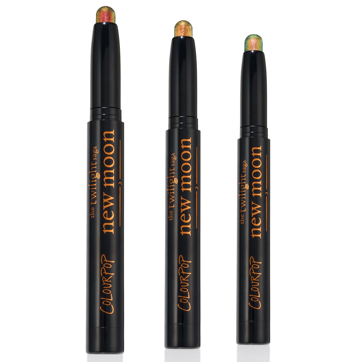 Love Triangle trio of ColourPop Shadow Stix stand uncapped to display shimmery multichrome tips - copper-red, golden bronze, and green-teal - in sleek black twist-up pens with The Twilight Saga New Moon branding, set against a clean white background.