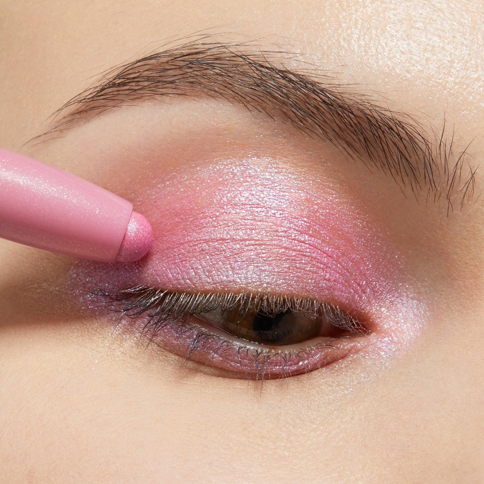 Juicy Gossip ColourPop Shadow Stix gliding over the eyelid, depositing shimmery bubblegum-pink color with a pearly finish; a tight eye close-up with natural brow showcases the creamy, blendable payoff.